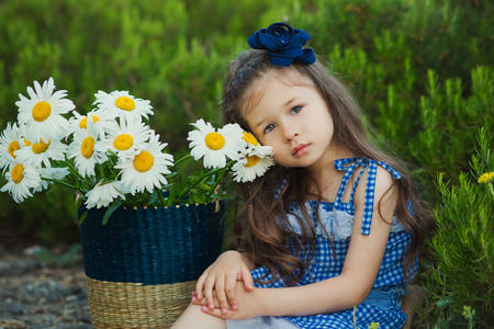 Young cute girl in jeans dress standing close to yellow flowers with basket full of chamomileの写真素材