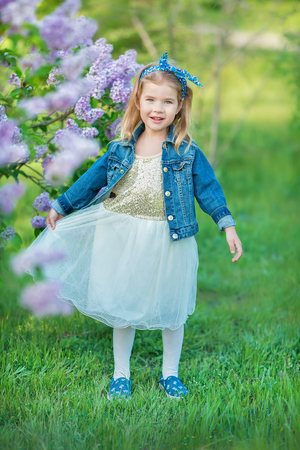 Cute girl in blue jackets with fairy airy skirt standing close to lilac bush.の写真素材