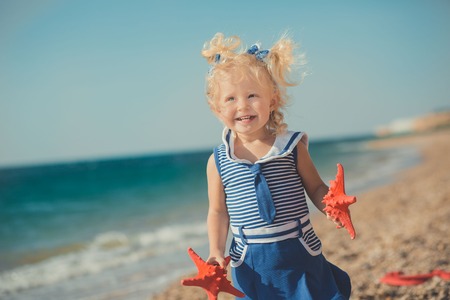 Cute girl on a sea side with two sea stars in blue dress.の写真素材