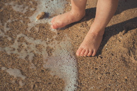 Child legs in a sand beach in summer time.