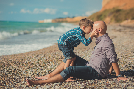 Weekend at the beach Dad and son sitting on the beach and looking at each other. A beach Stone sea foam pedigree.の写真素材