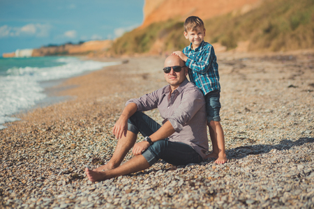 Weekend at the beach Dad and son sitting on the beach and looking at each other. A beach Stone sea foam pedigree.の写真素材