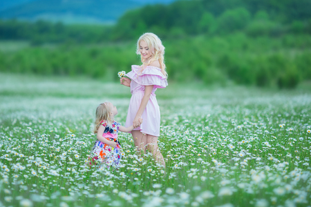 Blond mother with cute little daughter wearing white colourful pink dresses in chamomile field, summer time. Enjoying spending time together happy childhood.の写真素材