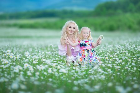 Blond mother with cute little daughter wearing white colourful pink dresses in chamomile field, summer time. Enjoying spending time together happy childhood.の写真素材