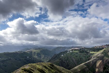 View of the hilltop on a mountainous landscape of volcanic origin along with lots of trees on the horizon, one can see the setting moon of the Gran Canary islandの写真素材