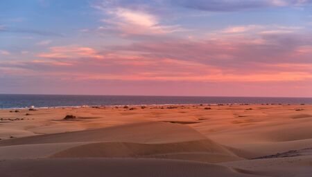 People passing through sand dunes overlooking the ocean on the horizon during a sunny day with thick clouds moving in the sky from the Grand Canary Islandの写真素材