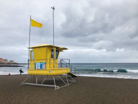 View of lifeguard tower on beach during windy sunny day with sea view and unique beach which has black sand on tower flutters green and yellow flag.の写真素材