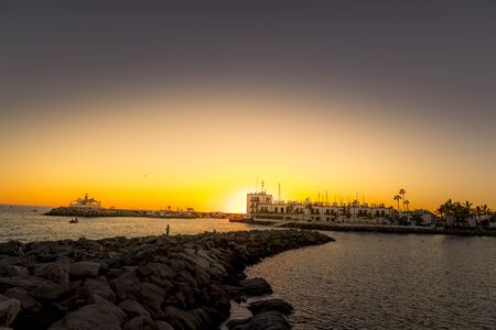 Sunset on the stony coast where fishermen are located during fishing with boats on the horizon and sunlight behind the city buildings from the Grand Canary Islandの写真素材