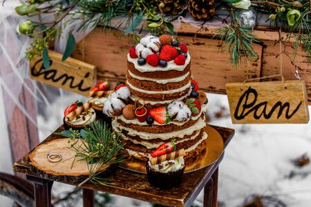 Wedding cake with fruit and an old wooden table with decorations and rings during a wedding ceremony in winter on snow in the middle of a forest covered with fresh snowの写真素材