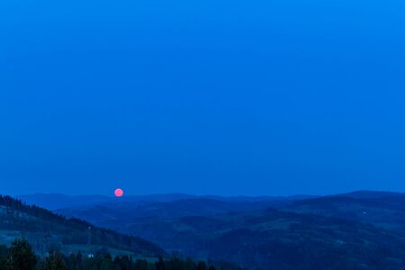 Red moon rising from a mountain area after sunset.の写真素材