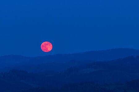 Red moon rising from a mountain area after sunset.