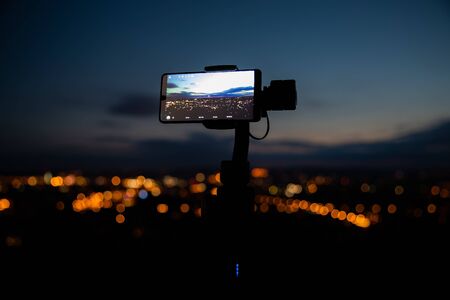 Mobile phone taking pictures on colorful sunset on Bila Hora with amazing view on city Brno Czech...
