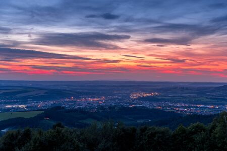 The setting sunset over the town of Valasske Mezirici as the city and its surroundings public light up slowly multi colored dark clouds and sun hiding below horizon.の写真素材