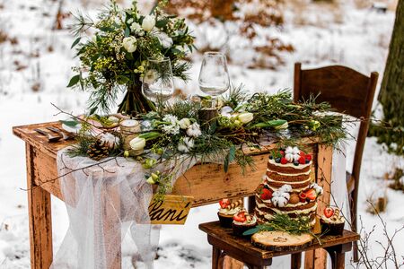 Wedding cake with fruit and an old wooden table with decorations and rings during a wedding ceremony in winter on snow in the middle of a forest covered with fresh snowの写真素材