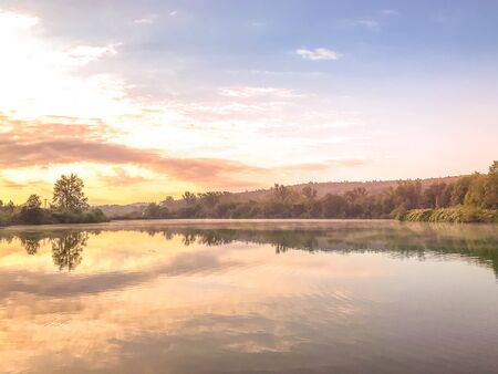 Sunset capture on the pond at the morning sunrise over trees lying near water and moving clouds over...