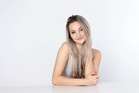Studio portrait of a pretty young blonde woman, wearing light dress, smiling and looking at the camera, against plain studio backgroundの写真素材