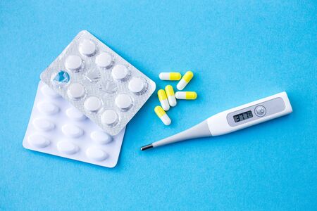 digital thermometer with 37,7 Â°C of temperature with pills in yellow/white capsules on blue...