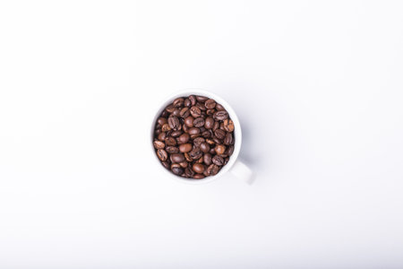 top view of White cup filled with freshly roasted coffee beans isolated on white backgroundの写真素材