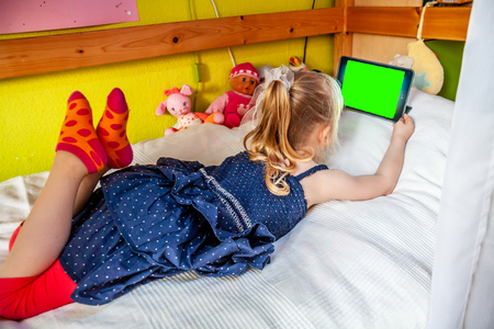 Cute little girl lying on bed and using her tablet computerの写真素材