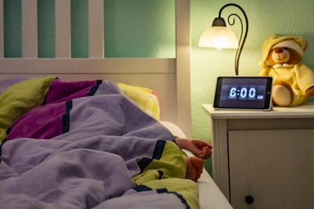 Little girl sleeping in bed - Alarm clock at 6 am in the morning.の写真素材