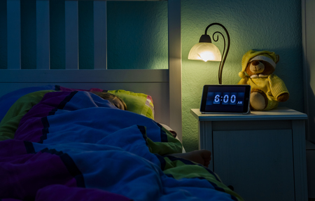 Little girl sleeping in bed - Alarm clock at 6 am in the morning.の写真素材