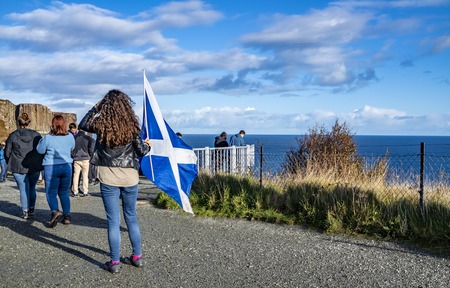 Isle of Skye / Scotland - October 14 2018 : Tourists visiting the Kilt Rock waterfall by Staffin with a waving flagのeditorial素材