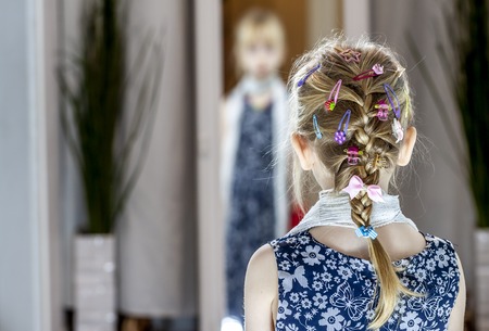 Little girl in the mirror at home wearing a skirt, scarf and shoes of motherの写真素材