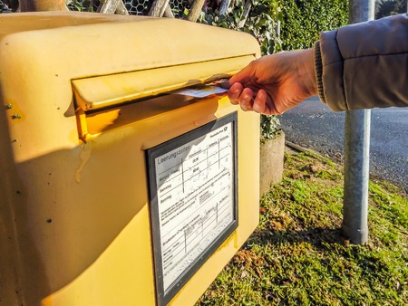 Moers / Germany - January 18 2019 : Lady throwing a letter into the standard yellow letterbox of...