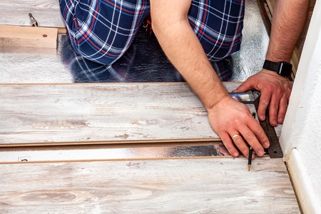 Man using measuring elbow and pencil while installing new wooden laminate flooring at home.