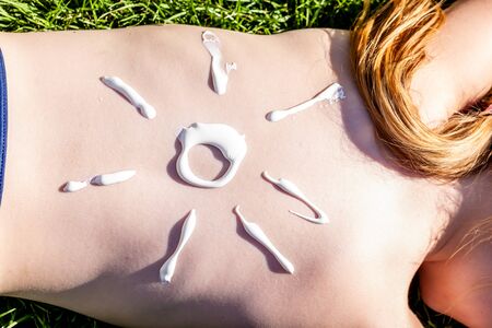 Sunscreen sun tan lotion sun drawing on girls back. Girl lying on the grass and sleeping.の写真素材