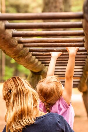 Mother Supporting daughter in the playground with climbing and hanging on a ladder