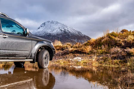 DUNLEWEY / IRELAND - FEBRUARY 13 2020 : Pickup standing in lake with the snow covered Errigal in...