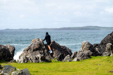 Man standing at a blowhole with water fountains at the beautiful coast next to Carrickabraghy Castle...