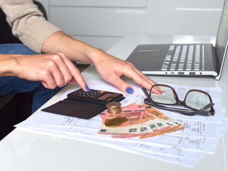 Woman using a calculator doing a balance of monthly expenses. There is money in euro on the table....