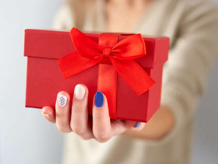 Female hand hold a red gift box. Birthday and Christmas gift with a red bow and ribbon. Giving a...
