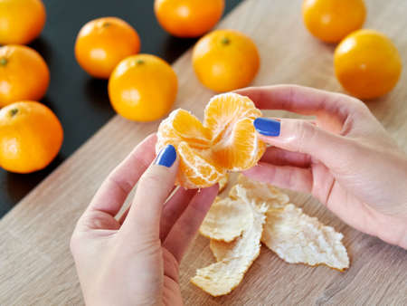 Mandarin peeling. Female hands peel the fresh orange fruit. Citrus fruits lying on the table....