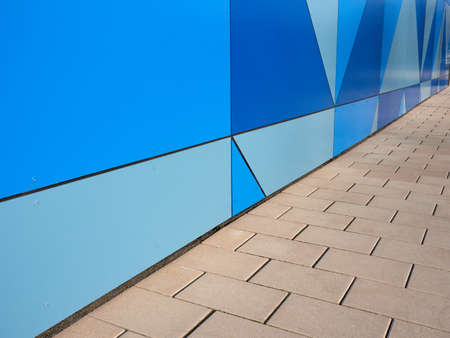The wall of the building with geometrical figures in shades of blue and a pavement. Modern, urban architecture. Background with triangles and squares.の写真素材