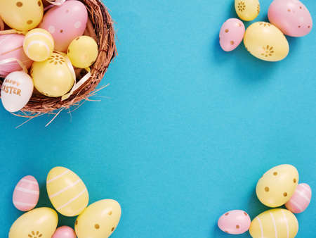 Flat lay composition of yellow and pink easter eggs in basket blue background with space for text.の写真素材