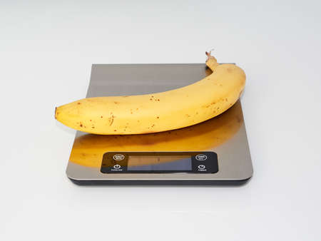 Yellow, ripe banana on the kitchen scale. White backgroundの写真素材
