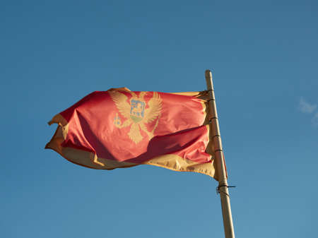The Montenegrin flag hung on a mast and fluttering in the wind against the backdrop of a blue sky.の写真素材