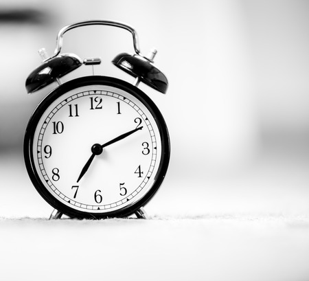 Still life black vintage alarm clock shows 7 am on bright bokeh background with copy space. Retro alarm clockの写真素材