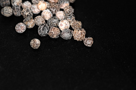 A close-up of whole unground black peppercorn - isolated on dark backgroundの写真素材