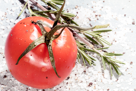 Red tomato with rosemary, cracked black pepper and sea salt on a vintage plateの写真素材