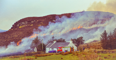 Dunvegan/Scotland, March 2014: Fire brigade trying to control a dry grass and reeds fire near residential buildingsのeditorial素材
