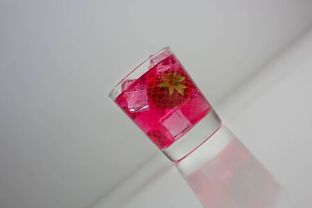 Strawberry juice extract poured into glass of water on white backgroundの写真素材