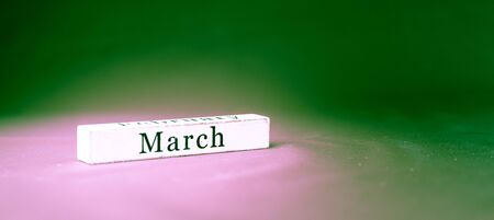 March, name of the month written on vintage white wooden block on green textured background . Banner format.の写真素材