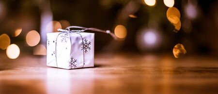 Close up of a gift box and fairy lights near decorated christmas tree over wooden floor background...