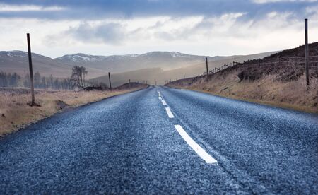 Road Trip in Scotland - black tarmac road with mountains and moorlands in the backgroundの写真素材