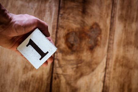 Number 1 - a hand holding a white block with number one over vintage wooden tableの写真素材