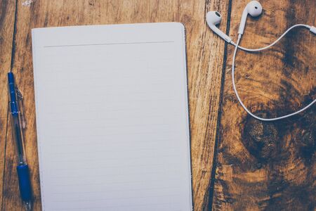 Writers work space - Blank notebook with pen on top of wood office desk table. White earphones next to it. Top view, flat lay. retro effect. Vintage styleの写真素材